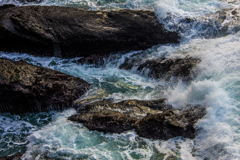 Turquoise ocean water washing and surging over dark textured coastal rocks from above